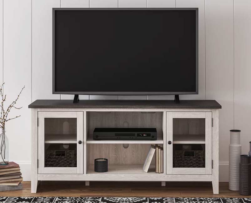 A minimalist designed living space with a large black flat-screen TV atop a two-tone wood and white media console with glass doors, complemented by simple decor and a patterned black and white rug below.